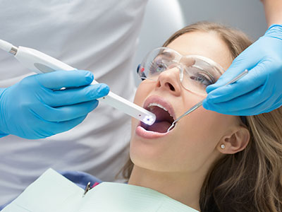 The image shows a dental professional using a device to clean a patient's teeth during a dental appointment.